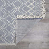Close up of the Ramsbury Denim Blue Wool Rug showing geometric pattern, fringe detail, and backing. Fold