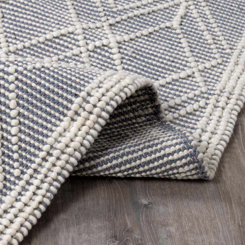 Close-up of the hand woven Ramsbury Denim Blue Wool Rug, showing its geometric pattern and textured wool and cotton blend. Fold