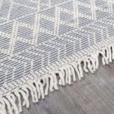Close-up of the Ramsbury Denim Blue Wool Rug featuring a geometric pattern and ivory fringe detail. Corner
