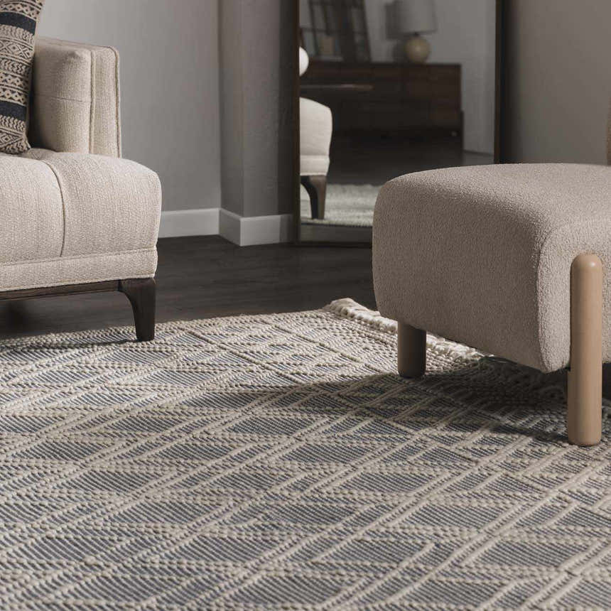 Living room scene with a Ramsbury Denim Blue Wool Rug, beige armchair, and ottoman. Geometric pattern. Roomscene-Rectangle