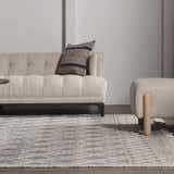 Living room scene with a Ramsbury Denim Blue Wool Rug, beige sofa, patterned pillow, and ottoman. Roomscene-Rectangle