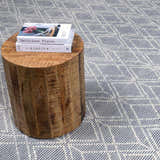 Close-up of the Ramsbury Denim Blue Wool Rug with geometric pattern and a wooden side table with books. Styleshot