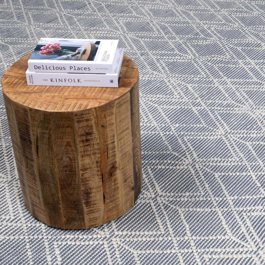 Close-up of the Ramsbury Denim Blue Wool Rug with geometric pattern and a wooden side table with books. Styleshot