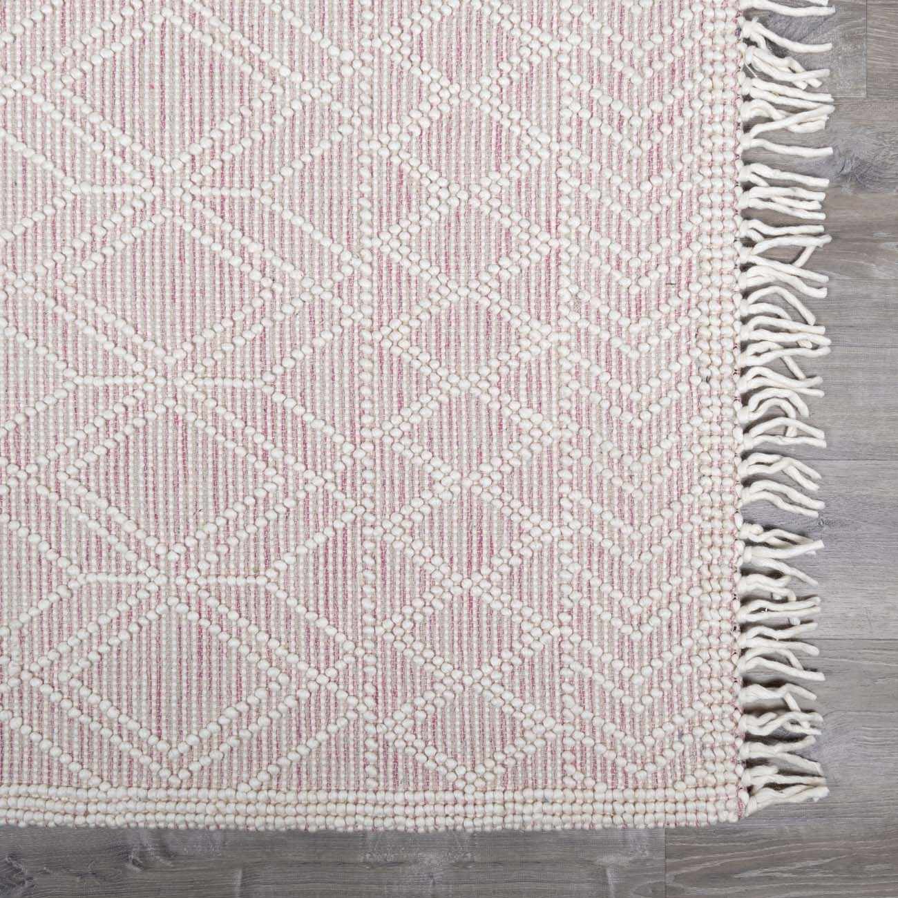 Close-up of the Ramsbury Soft Pink Wool Rug. Features a geometric pattern, fringe, and pink and ivory hues. Swatch