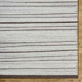 Close-up of the hand-tufted Cliona Area Rug. Wool rug with charcoal, ivory, and taupe horizontal stripes. Corner
