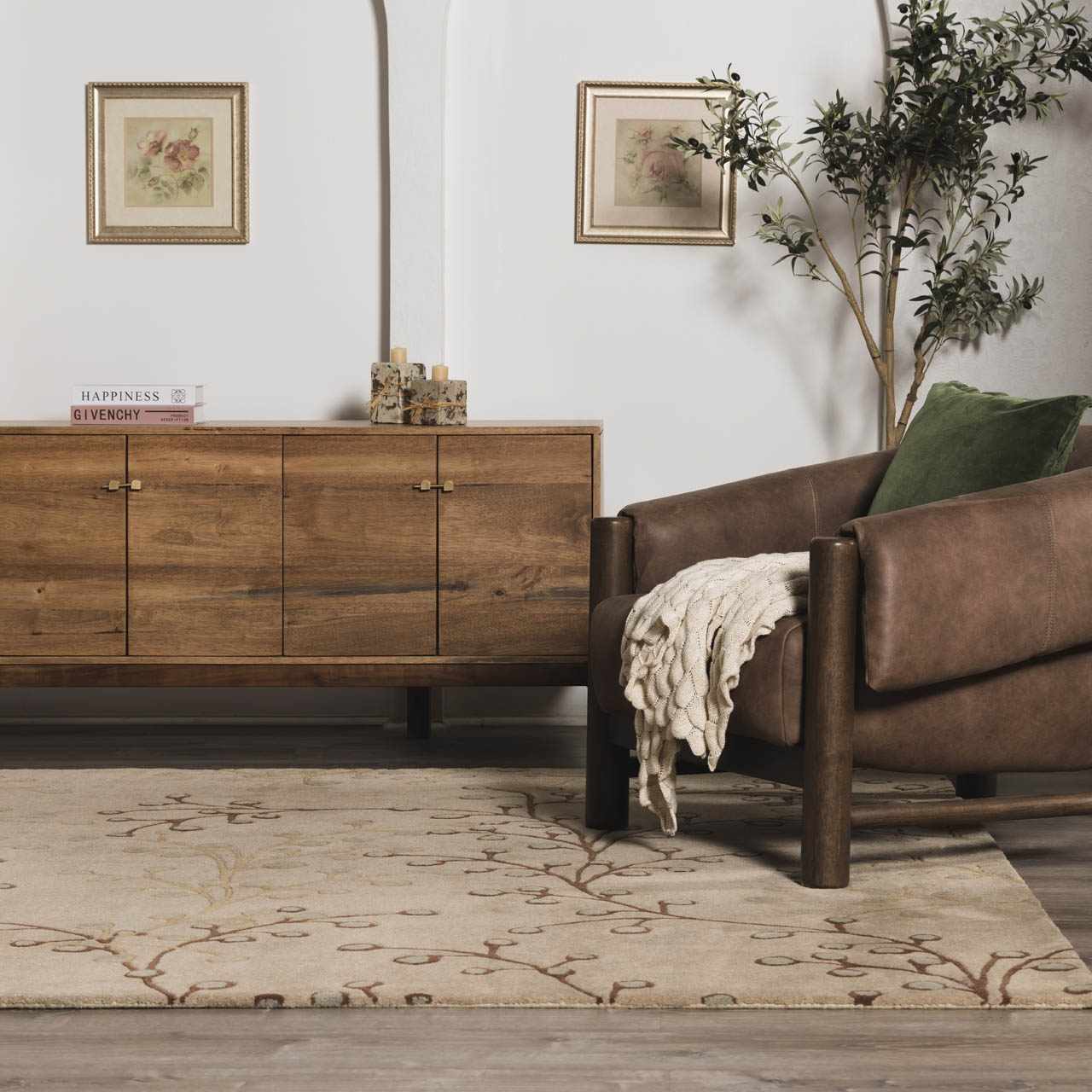 Living room scene with a beige Elsu Wool Rug, brown leather chair, and wooden cabinet. Floral art on the wall. Roomscene-Rectangle