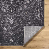 Close-up of the Corina Black Area Rug showing its traditional floral pattern and gray, ivory, and charcoal colors. Fold
