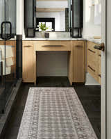 Bathroom scene with a Rainier Light Brown Washable Rug, light wood vanity, black herringbone tile floor, and glass shower. Roomscene-Runner