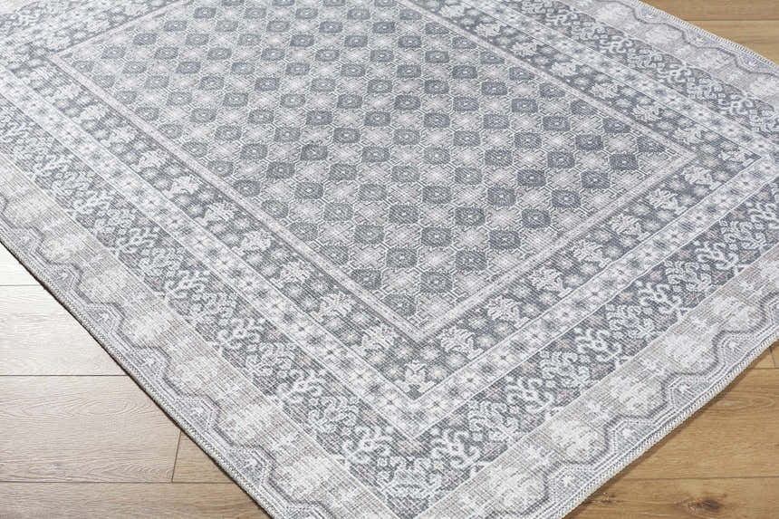Close-up of the Rainier Gray Washable Rug. Farmhouse style rug with off white, pale blue, sage, and tan traditional pattern. Corner