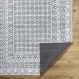 Close-up of Rainier Gray Washable Rug showing its traditional pattern, off white, pale blue, sage, and tan colors. Machine woven texture. Fold