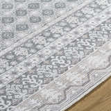 Close up of Rainier Gray Washable Rug showing farmhouse style pattern in off white, pale blue, sage, and tan colors. Texture