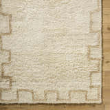 Close-up of the hand-tufted Ciniod Area Rug. The rug is pearl and tan with a geometric pattern and a soft, wool texture. Corner