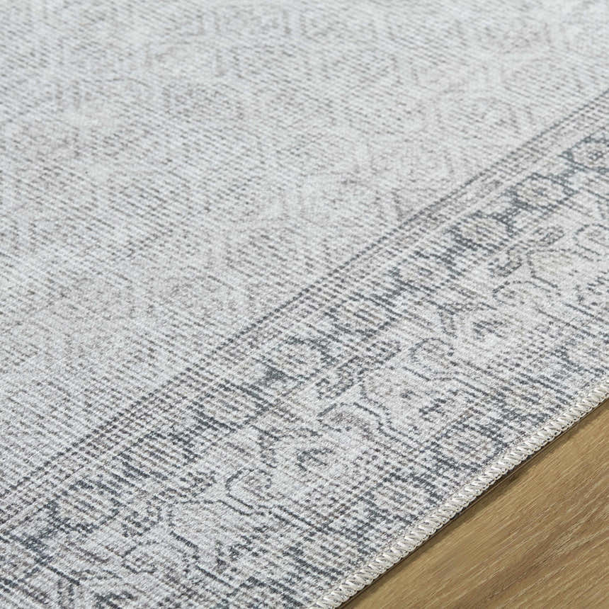 Close-up of the Rainier Cottage Border Gray Washable Rug, showing its gray and off-white traditional pattern and woven texture. Texture