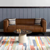 Living room scene with a brown leather sofa and the New Southfields area rug in aqua, peach, and mustard colors. Roomscene-Rectangle