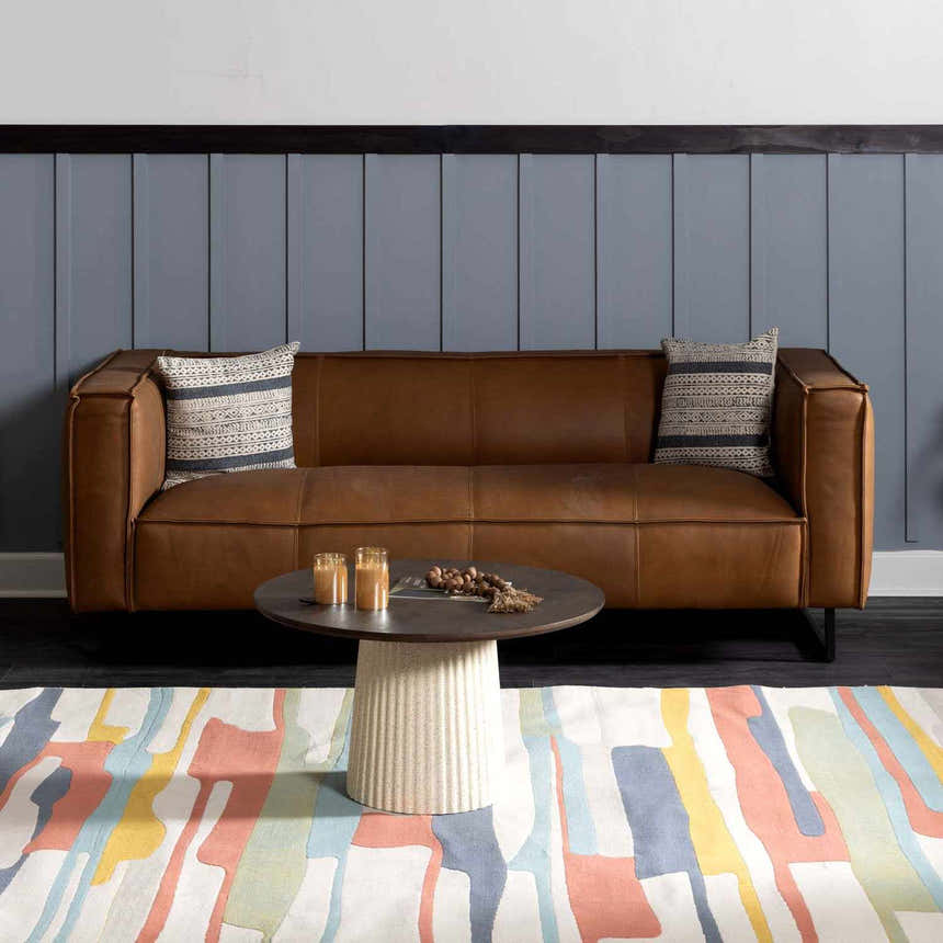 Living room scene with a brown leather sofa and the New Southfields area rug in aqua, peach, and mustard colors. Roomscene-Rectangle