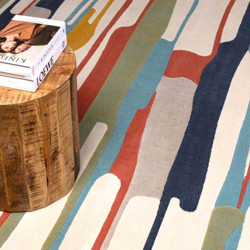 Close-up of the New Southfields rug. Abstract design in aqua, charcoal, mustard, orange, and gray. Wood side table with books. Styleshot