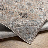 Close-up of the Civankan Area Rug. Traditional oriental pattern in brick red, denim, dusty sage, and brown on a wood floor. Fold