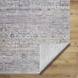 Close-up of the Cemile Area Rug showing its black, gray, ivory, and taupe traditional pattern and texture on wood floor. Fold
