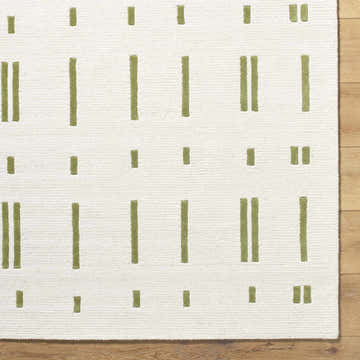 Close up of the Charan Ivory Area Rug featuring a contemporary olive dash pattern on a soft wool texture. Corner