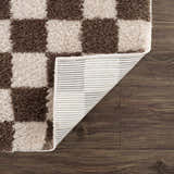 Close-up of a Canika Brown Washable Checkered Area Rug showing dark brown and peach squares, plus rug backing. Fold