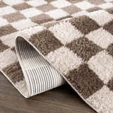 Close-up of the Canika Brown Washable Checkered Area Rug, showing dark brown and peach squares and the rug's backing. Fold