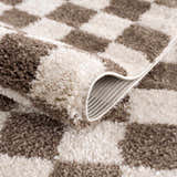 Close-up of the Canika Brown Washable Checkered Area Rug showing its dark brown and peach checkered pattern and soft texture. Fold