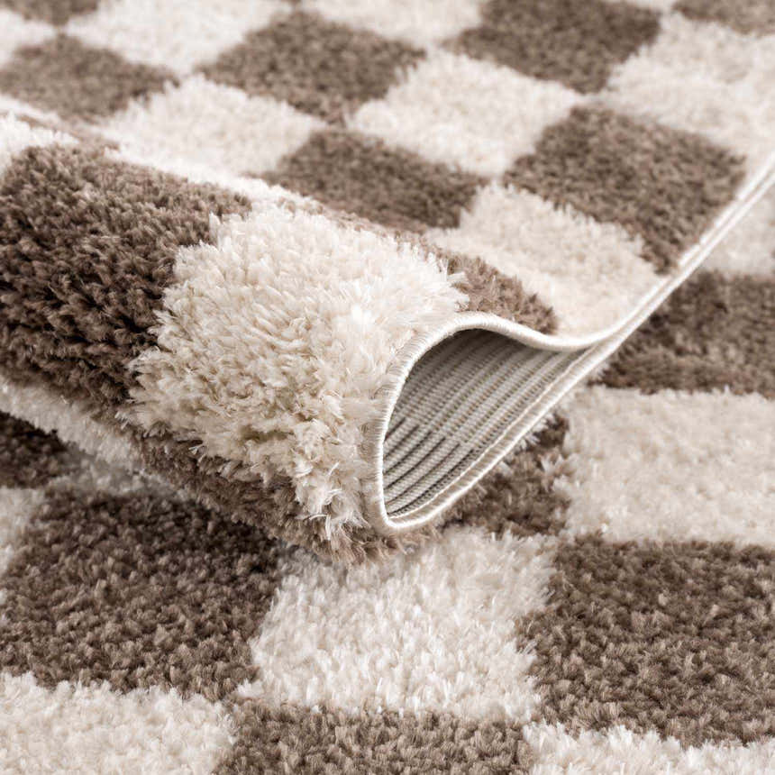 Close-up of the Canika Brown Washable Checkered Area Rug showing its dark brown and peach checkered pattern and soft texture. Fold