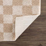 Close-up of the Canika Checkered Cream Washable Area Rug showing beige and peach tones and the rug's backing. Fold