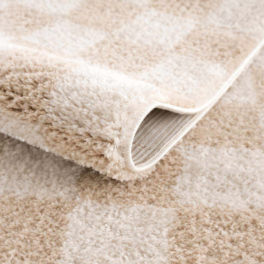 Close-up of the plush Canika Checkered Cream Washable Area Rug. Beige and peach checkered pattern with a soft, textured pile. Fold