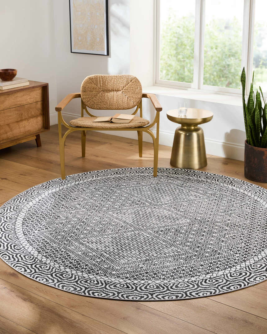 Living room scene with round Coledale Black & White Washable Rug, straw chair, wood dresser, and gold side table. Roomscene-Round