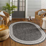 Cozy porch scene with an oval Coonamble Bordered Antrasit Rug, wicker chairs, and wood floors. Roomscene-Oval