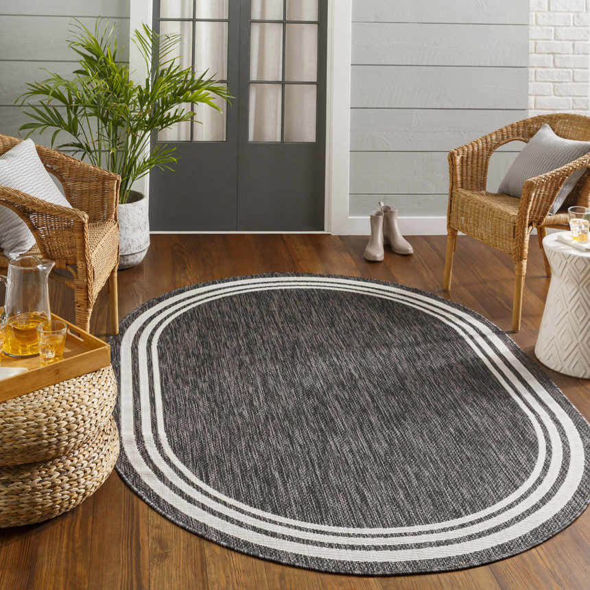 Cozy porch scene with an oval Coonamble Bordered Antrasit Rug, wicker chairs, and wood floors. Roomscene-Oval