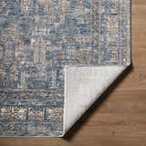 Close-up of the Mirabel Denim Blue Traditional Rug showing its texture, colors, and folded corner on a wood floor. Fold