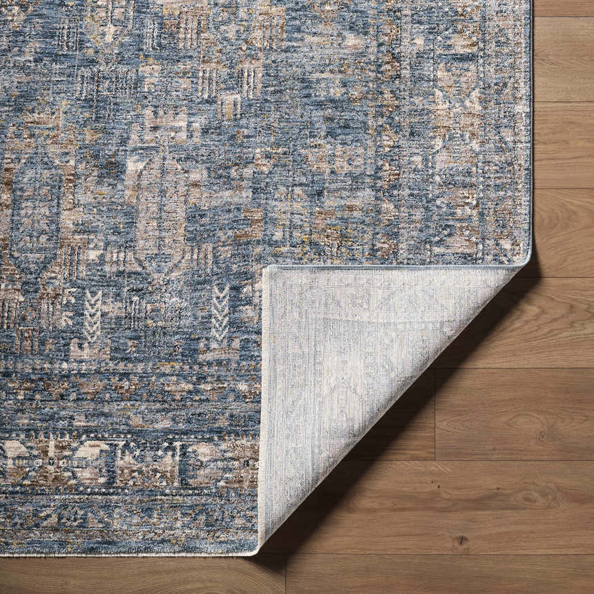 Close-up of the Mirabel Denim Blue Traditional Rug showing its texture, colors, and folded corner on a wood floor. Fold