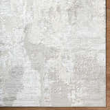 Close-up of the textured Chroma Abstract Cream Area Rug with ivory, light gray, and white tones on wood flooring. Corner