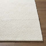 Close-up of the textured Cqasce Navy Solid Hand Woven Wool Area Rug in off-white on a wood floor. Front