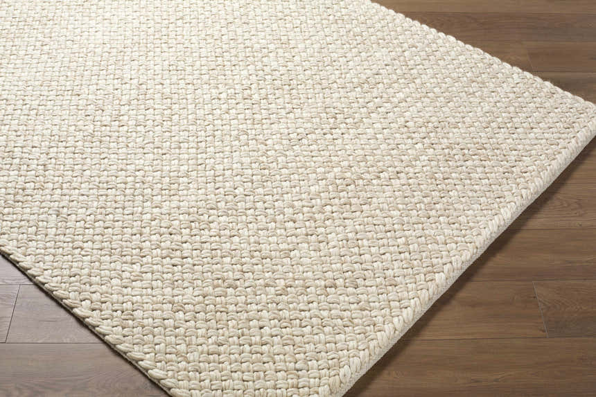 Close up of the hand woven texture of the Rowue Ivory Solid Wool Area Rug on hardwood floor. Corner
