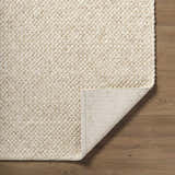 Close-up of the hand woven texture of the Rowue Ivory Solid Wool Area Rug on hardwood flooring. Fold