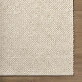 Close-up of the hand woven texture of the Rowue Ivory Solid Wool Area Rug on wood floor. Corner