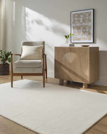 Living room scene with ivory Callie Area Rug, gray armchair, and wood cabinet. Modern, neutral tones. Roomscene-Rectangle
