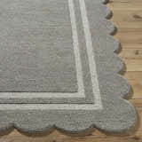 Close-up of the Chogan Stone Gray Area Rug. Features a scalloped edge and light gray stripes on a wood floor. 100% Wool. Front