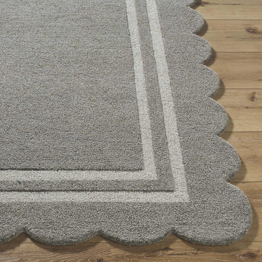 Close-up of the Chogan Stone Gray Area Rug. Features a scalloped edge and light gray stripes on a wood floor. 100% Wool. Front