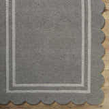 Close-up of hand-tufted Chogan Stone Gray Area Rug. Features a gray wool pile, light gray border, and scalloped edge detail. Corner