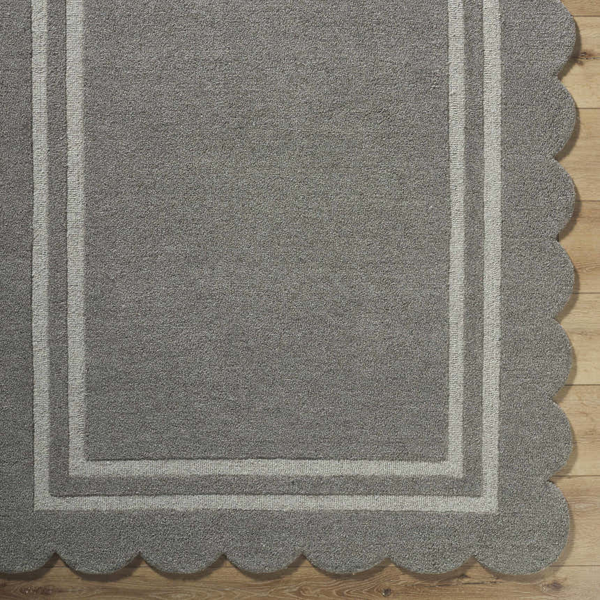 Close-up of hand-tufted Chogan Stone Gray Area Rug. Features a gray wool pile, light gray border, and scalloped edge detail. Corner
