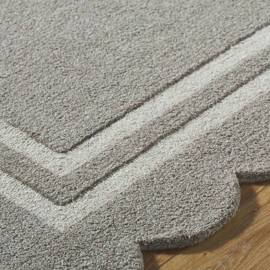 Close-up of the hand-tufted Chogan Stone Gray Area Rug showing its wool texture, geometric border, and scalloped edge. Texture