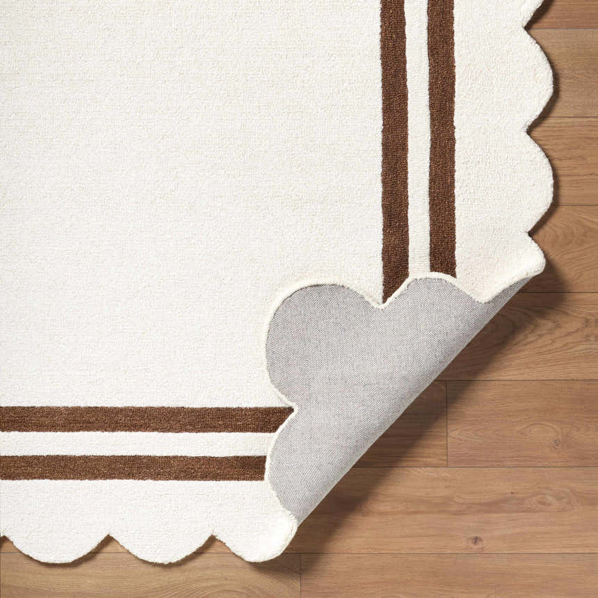 Close-up of the Chogan Ivory Area Rug showing the scalloped edge, brown stripes, and rug backing on wood floor. Fold