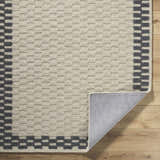 Close-up of the hand-tufted Camdyn Area Rug. Ivory wool rug with a charcoal checkerboard border on a wood floor. Fold