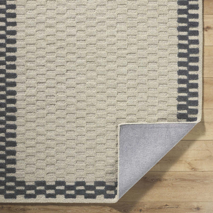 Close-up of the hand-tufted Camdyn Area Rug. Ivory wool rug with a charcoal checkerboard border on a wood floor. Fold
