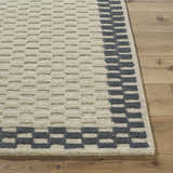 Close-up of the Camdyn Area Rug. Ivory rug with a charcoal geometric border on hardwood floor. 100% wool, hand tufted. Front