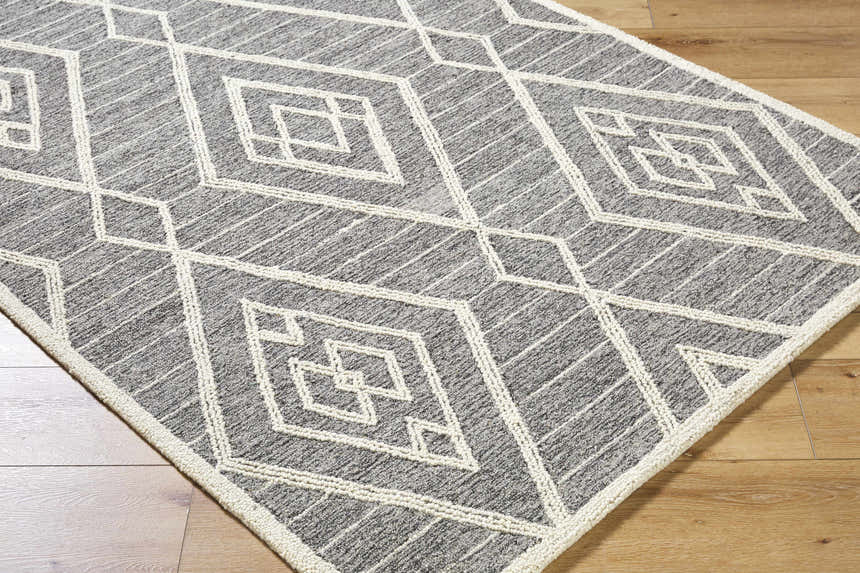 Close-up of the Ceanna Area Rug. Gray wool rug with off-white geometric diamond pattern on light wood floor. Corner